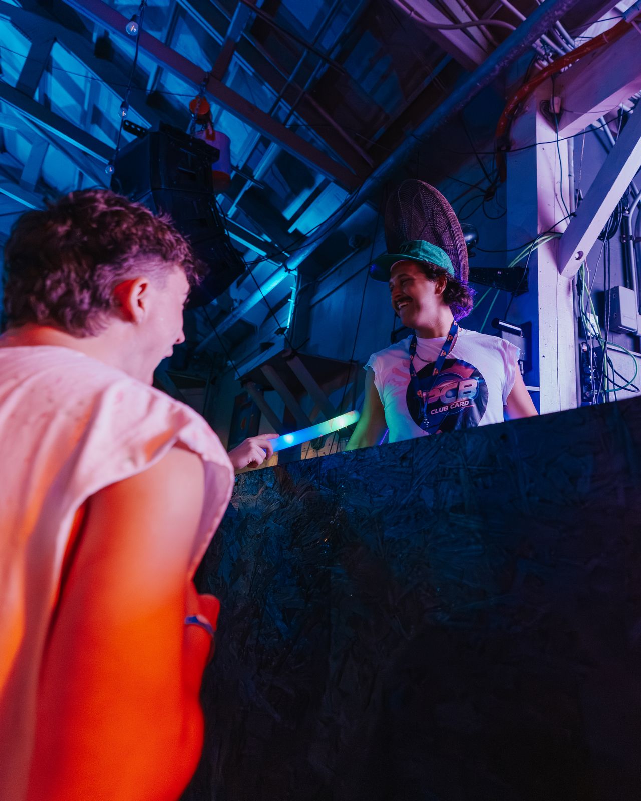 Two friends laughing at the edge of a DJ booth during a spring break night, Panama City Beach